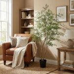 Cozy living room corner with a brown leather armchair, cream throw blanket, and two pillows beside a tall potted plant and wooden bookshelf.