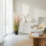 Bright living room with floor-to-ceiling windows, pampas grass plant, and a gray armchair with a beige throw.