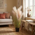 Living room with a potted pampas grass plant by a window, beige sofa with pink cushions, and a wooden bench with vases and a folded blanket.
