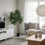 Tall potted plant beside a gray sofa in a bright modern living room with a white TV cabinet and wooden coffee table.