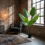 Cozy loft living space with a black leather armchair, brick wall, rug, and a tall leafy plant by a large window.