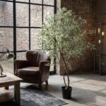 Cozy industrial living room with a leather armchair, wooden coffee table, and a tall potted plant near a brick wall.