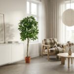 Bright living room featuring a tall potted plant beside a white cabinet, a plaid-armchair with throw, and a round coffee table by large windows.