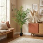 Cozy living room corner featuring a tall potted palm, a wooden bench with cushions, and a mid-century sideboard with vases and botanical art on the wall.