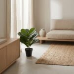 Minimalist living room corner: potted plant, beige sofa, wooden cabinet, and a woven rug in warm natural light.