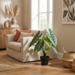 Cozy living room with a beige armchair, green potted plant, and woven rug near a window. A wooden cabinet and pampas grass decor are in the background.