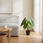 Living room corner with a gray sofa, round wooden coffee table, wicker basket, and a potted plant by a large window with sheer curtains.