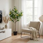 Bright living room corner featuring a potted lemon tree beside a beige lounge chair, a white media console, and a large window with sheer curtains.