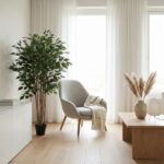 Bright living room with a tall potted plant, gray armchair, and light wood coffee table by sheer white curtains.
