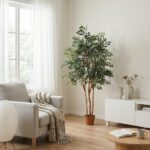 Bright living room with a tall potted plant beside a gray armchair and a white console, a cozy blanket draped over the chair and an open book on a round coffee table.