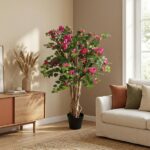 Potted flowering plant with pink blossoms in a sunlit living room corner, beside a beige sofa and wooden console table.