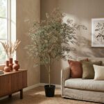 Tall indoor plant in a black pot beside a beige sofa with rust and cream cushions in a cozy living room.