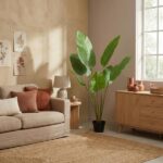 Living room with a beige sofa and rust cushions, tall green plant by a side table and wooden cabinet in natural light.