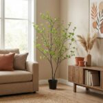 Living room with a tall potted plant beside a beige sofa, and a wooden console with vases and dried grasses on a sunny wall.