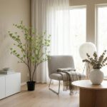 Bright living room corner with a tall potted plant, gray chair, and white round lamp near a window.
