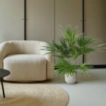Beige textured armchair beside a potted palm plant on a round jute rug in a neutral living room.