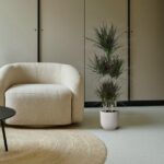 Beige boucle armchair beside a tall potted plant on a neutral-toned living room backdrop. 1/5