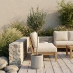 Small potted tree on a wooden deck next to beige outdoor seating and a stone wall patio area.