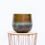 Glazed ceramic pot with brown top and turquoise speckled glaze sits on a round wooden table with a copper wire base.