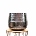 Hammered metallic planter sitting on a round wooden stool/table with hairpin legs