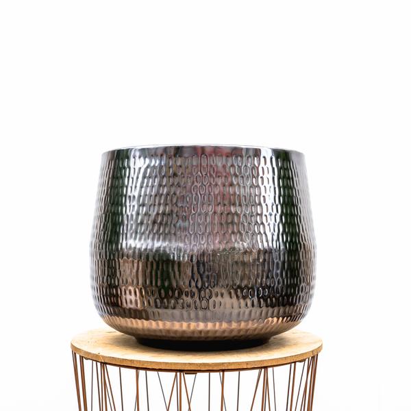Hammered metal planter with a bronze finish sitting on a round wooden stand with hairpin legs.