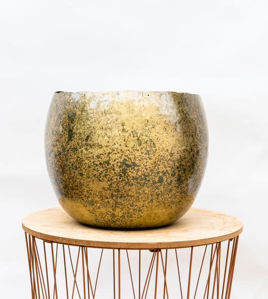 Round ceramic planter with a gold-green speckled glaze on a light wooden round pedestal with thin metal legs.