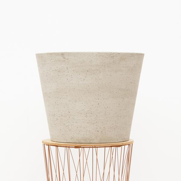 Beige speckled planter resting on a round wood plate atop a copper wire plant stand.