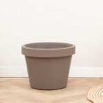 Large empty brown plant pot on a light wooden floor against a white wall.