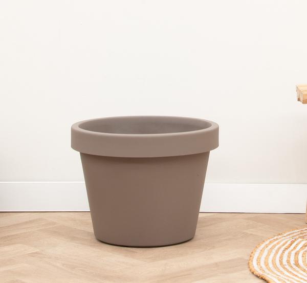 Large empty brown plant pot on a light wooden floor against a white wall.