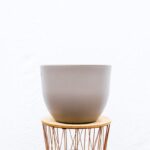 Gray ceramic plant pot on a round wooden saucer, set on a copper wire stand against a white background (empty pot).