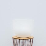 White ceramic bowl atop a wooden stool against a pale wall, minimalist still life.