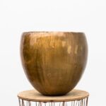 Brown glazed ceramic pot resting on a round wooden table in a bright studio setting against a white background.