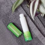 Opened lip balm stick on grey towels near green plant in bath l - Hidalgo
