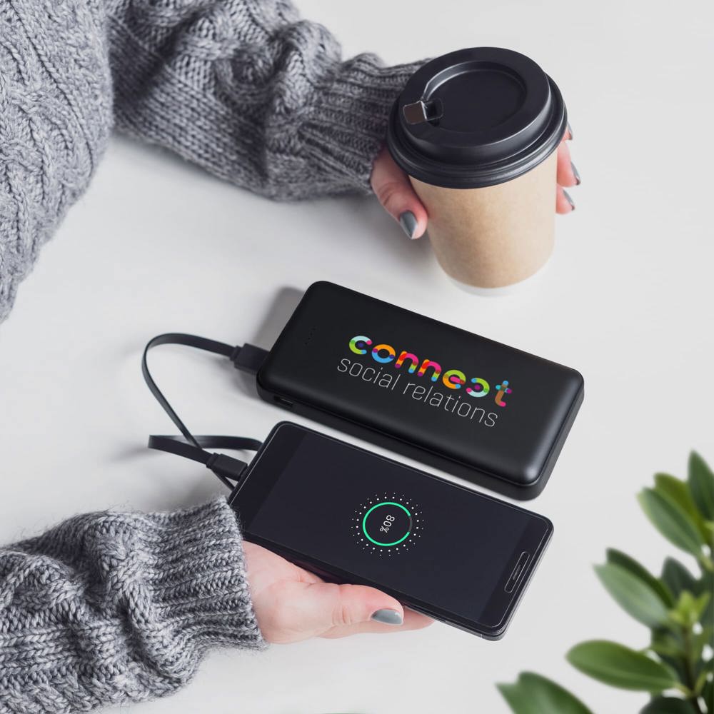 The girl drinks coffee uses the power bank charges the phone Modern technologies and portable chargers - Hidalgo